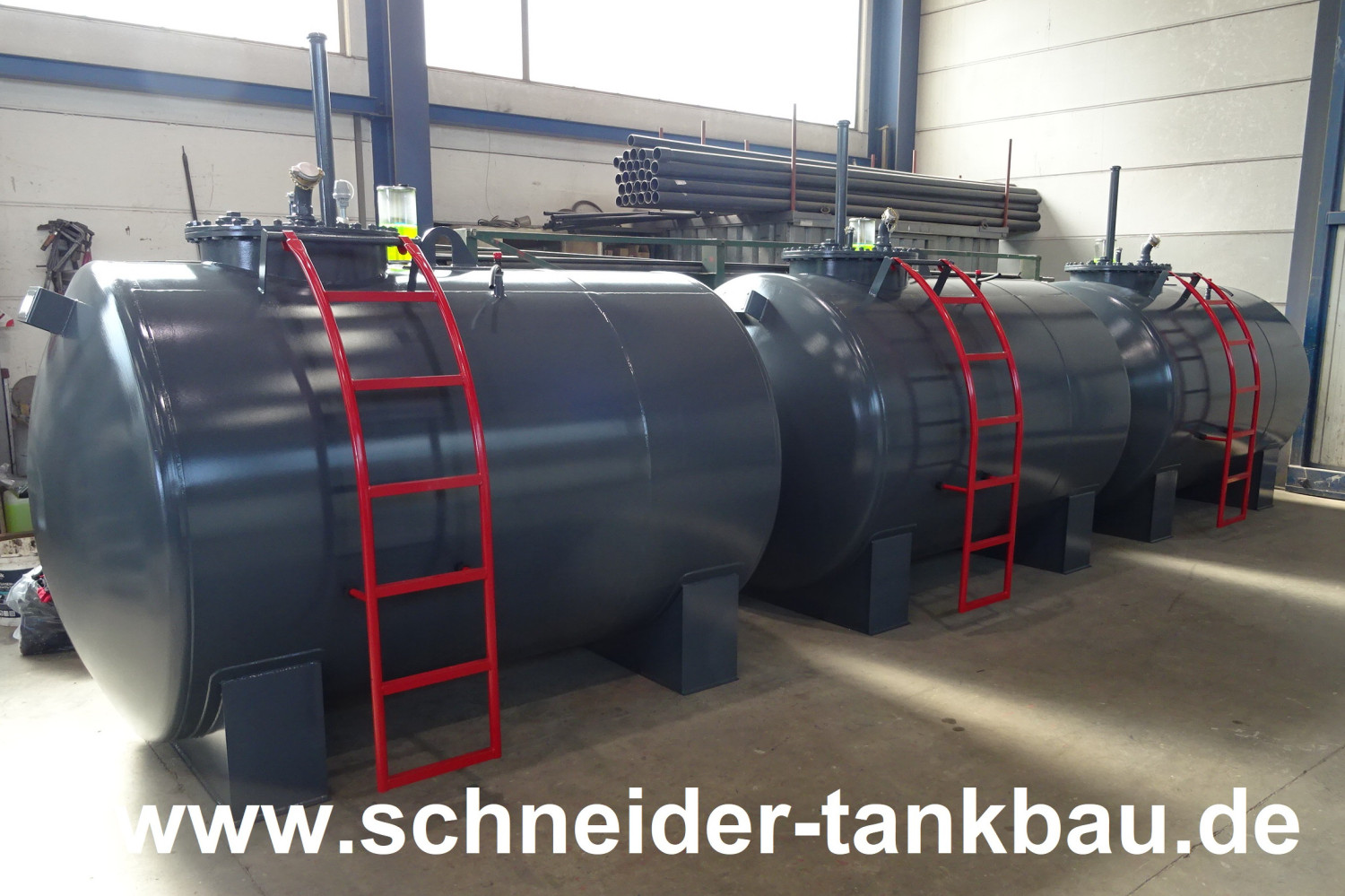 Drei baugleiche graue Heizöltanks mit roten Leitern und 5.000 Liter Fassungsvermögen in einer Halle.
