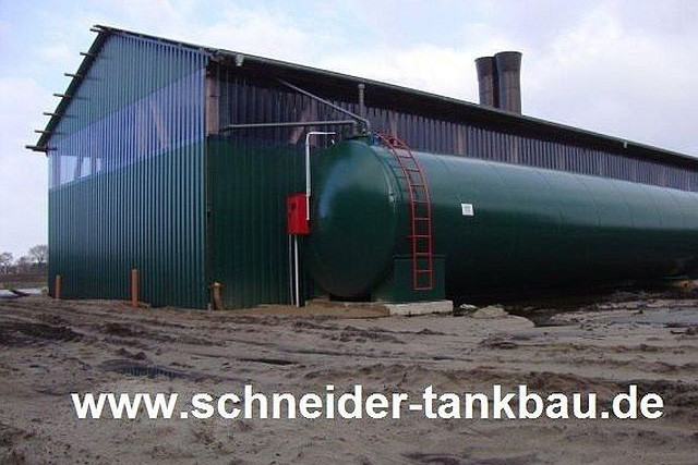 Grüner Flüssigdüngertank mit Anschlussrohren vor einer landwirtschaftlichen Halle.
