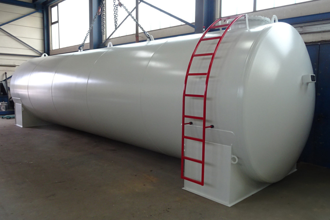 Großer silberner horizontaler Lagertank mit roter Leiter und Hebeösen in einer Industriehalle.