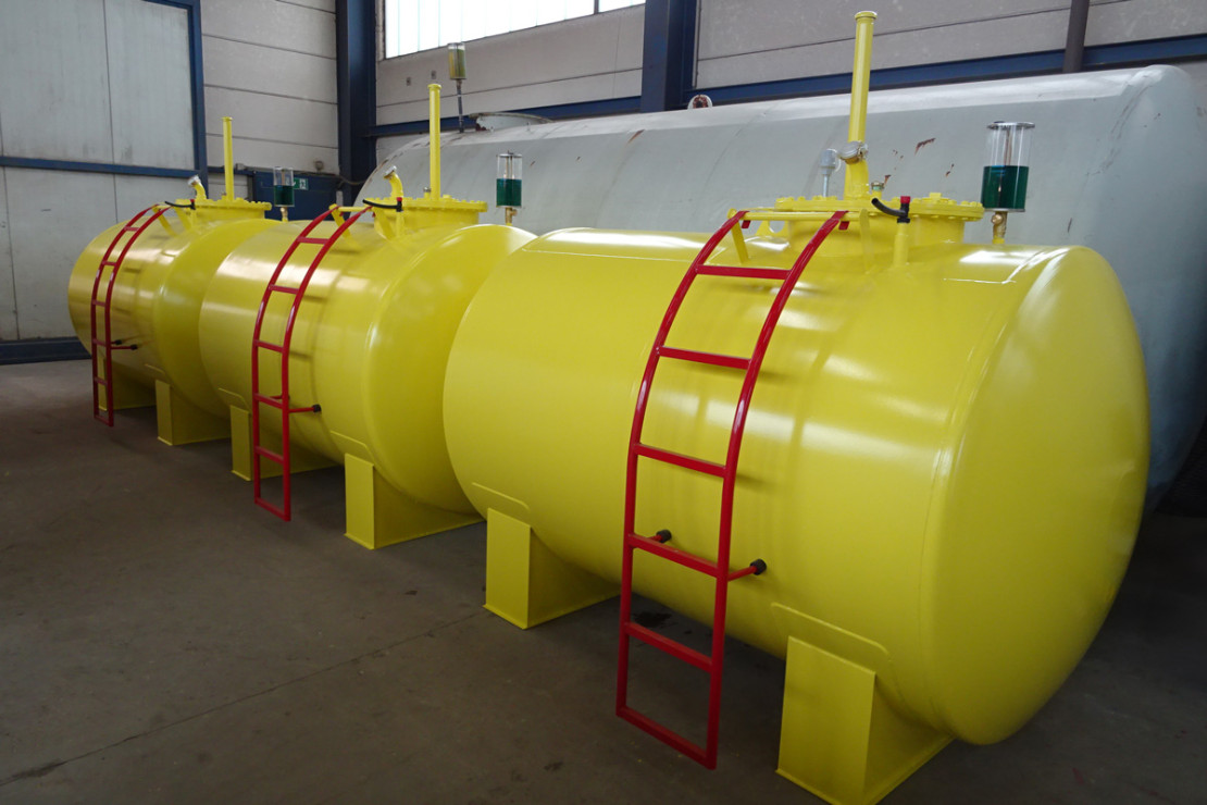 Zwei gelbe oberirdische Lagertanks mit roten Leitern und Entlüftungsrohren nebeneinander in einer Produktionshalle.