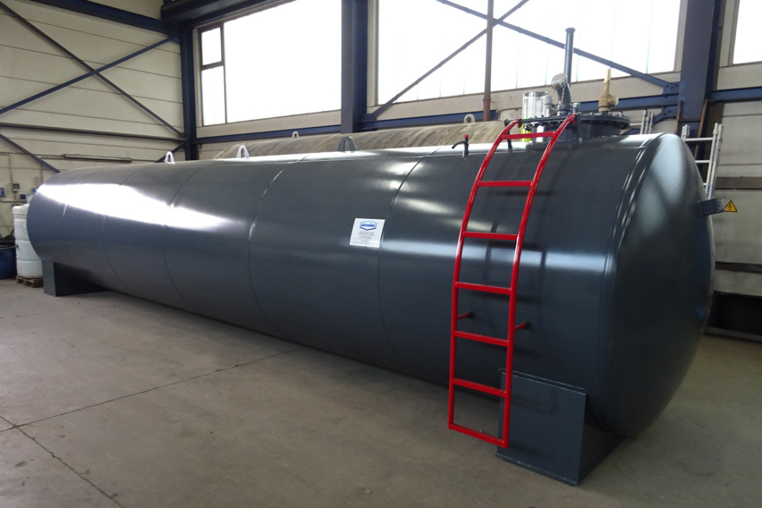 Großer anthrazitfarbener horizontaler Lagertank mit roter Leiter und Armaturen in einer Industriehalle