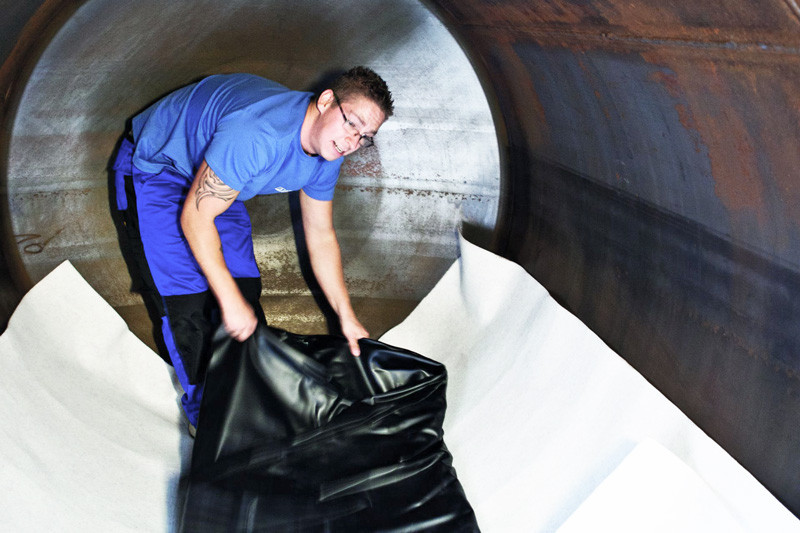Techniker verlegt eine schwarze Folie zur Tankinnensanierung im Inneren eines Stahltanks.