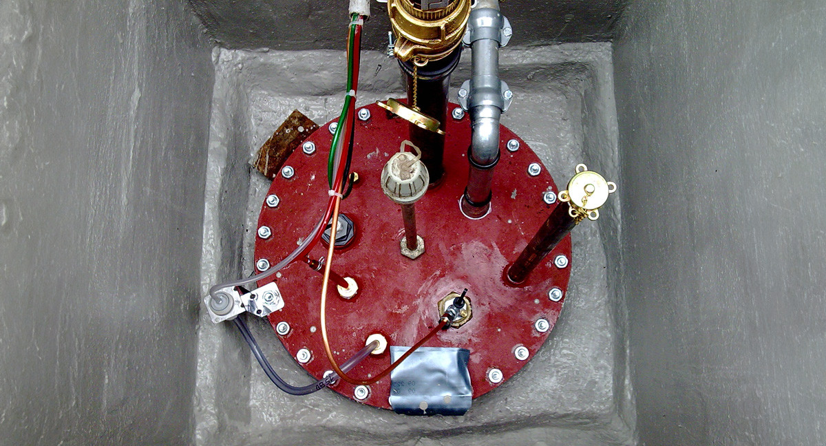Draufsicht auf einen roten Tankdeckel mit Rohranschlüssen, Kabeln und Armaturen eines Erdtanks