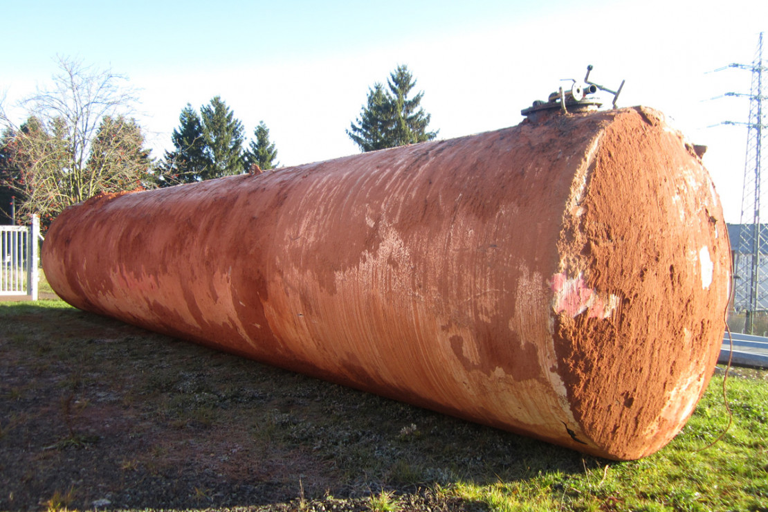 Zylindrisch liegender Erdtank liegt auf einer Wiese und ist noch mit Erde behaftet